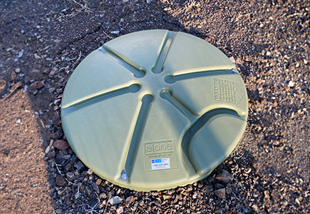 A photo of a pressure sewer system lid sticking out of the ground.